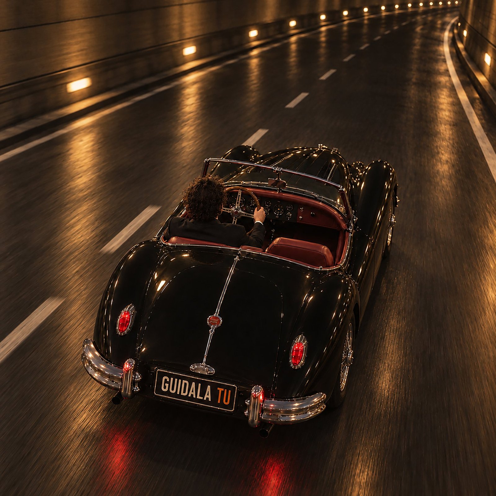 Una Jaguar roadster nera attraversa un tunnel illuminato di ambra; sulla targa la scritta Guidala tu.